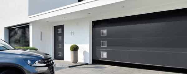 Exterior de una casa moderna con una puerta de garaje gris oscuro y un coche aparcado delante.