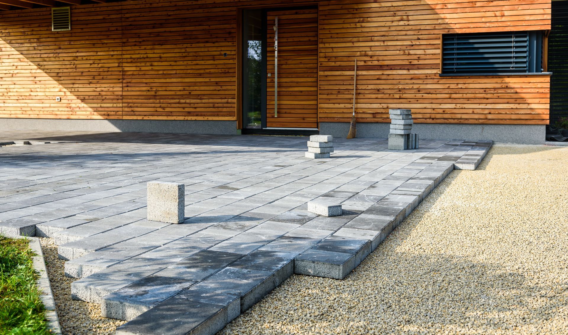Construction of a patio with gray pavers in front of a wooden house.