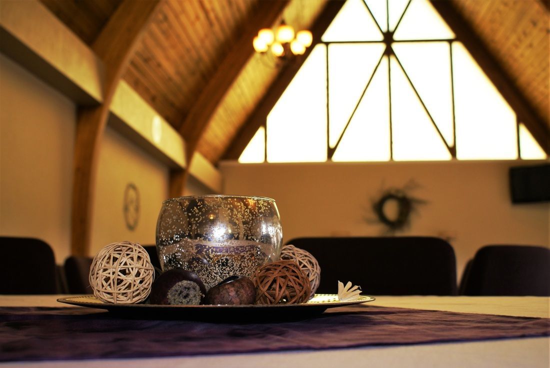 Glass candle holders on a table in a warmly lit room with a large triangular window.