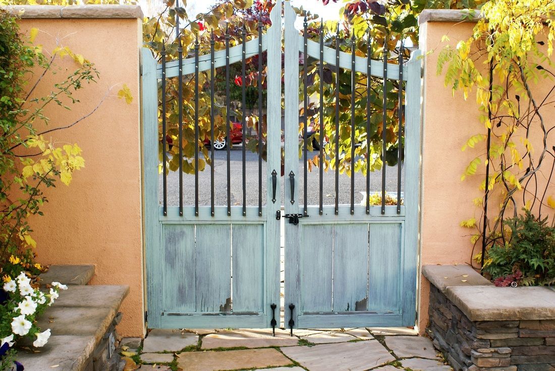 Light blue garden gate framed by peach walls, with flowers and stone steps in a sunny courtyard