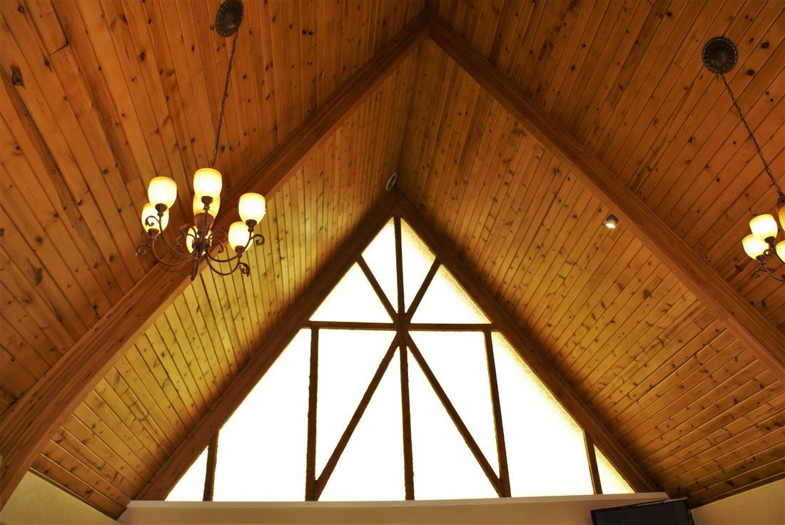 Wood-paneled cathedral ceiling with hanging chandeliers and a large triangular window