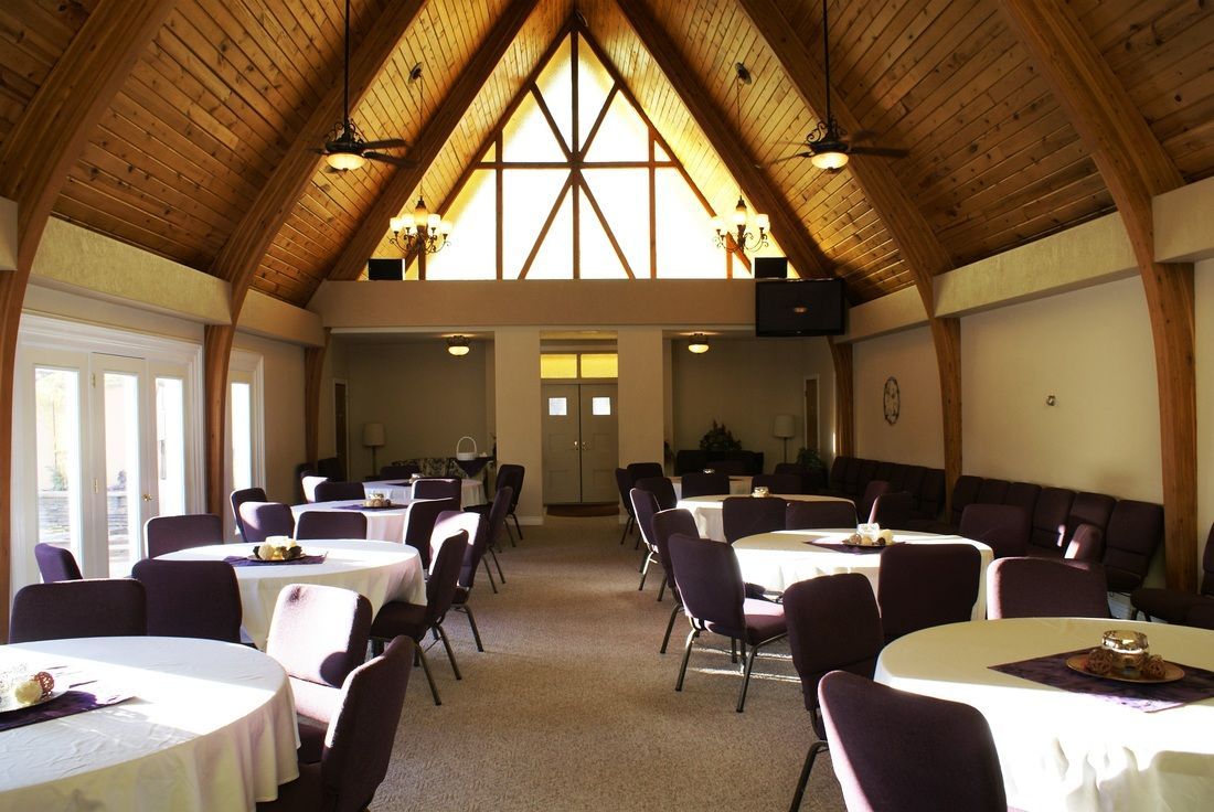 Dining room with round tables and purple chairs under a vaulted wooden ceiling.