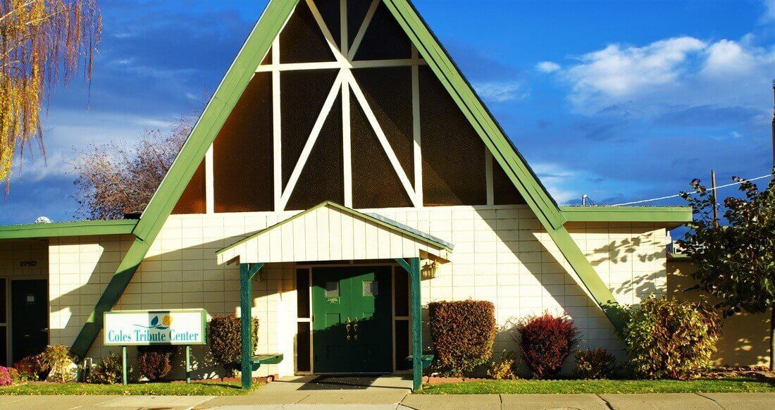 Small church building with a steep A-frame roof, green trim, and a covered front entrance under a blue sky