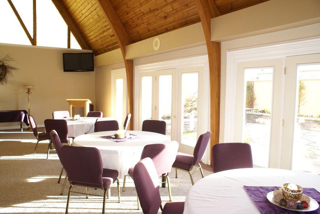Sunlit dining room with purple chairs, round tables, and large glass doors under a wooden ceiling