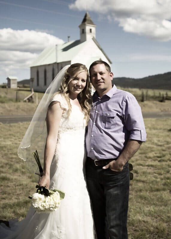 Bride and groom posing outside a white church on a sunny day