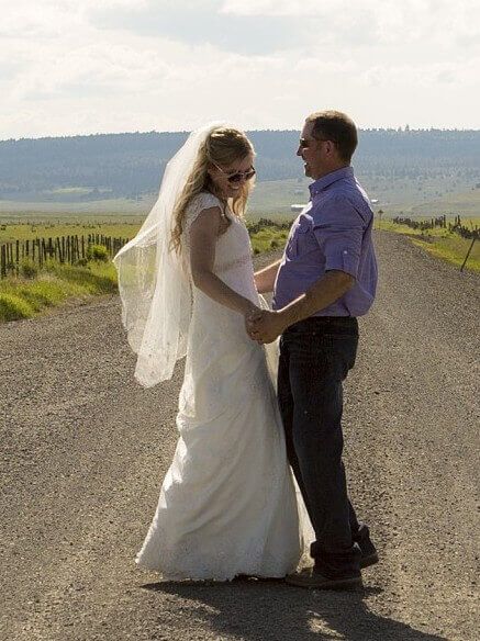 Bride and groom holding hands on a rural road with a veil flowing in the wind
