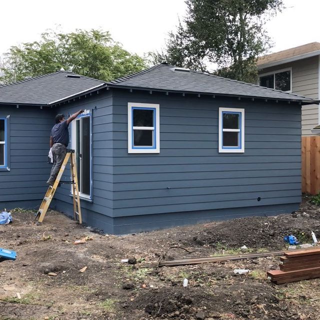 A man is painting the side of a blue house.