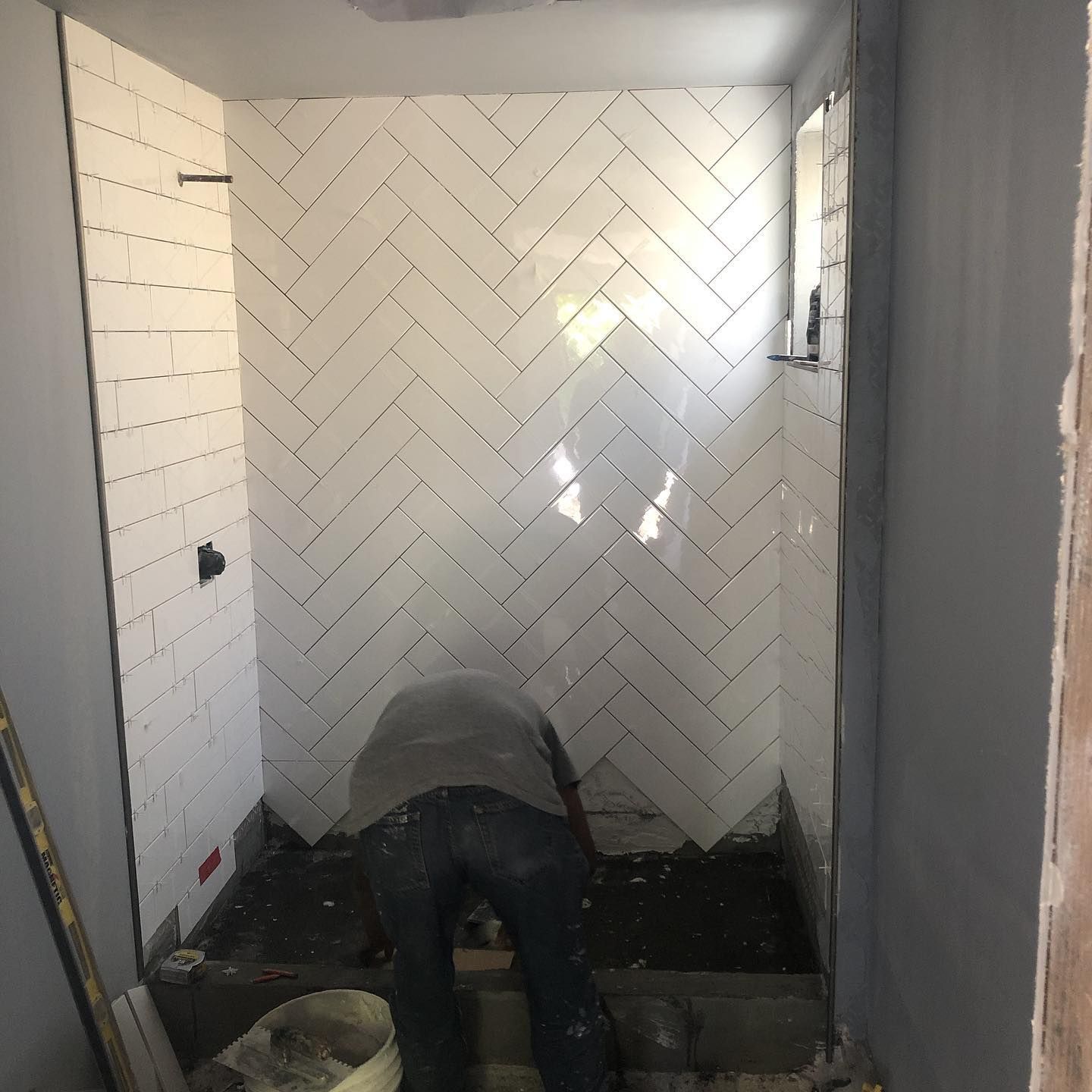 A man is working in a bathroom with a herringbone pattern on the wall.