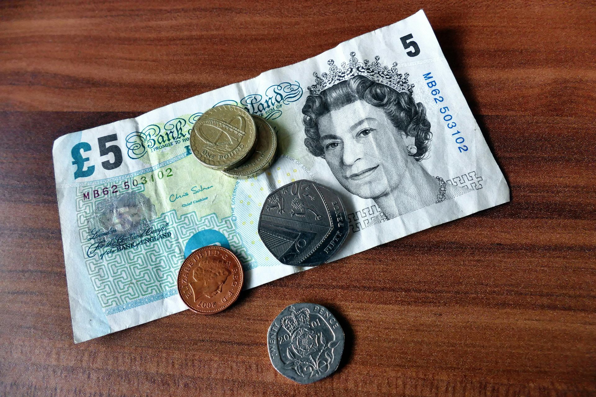 A 5 pound note and some coins on a wooden table