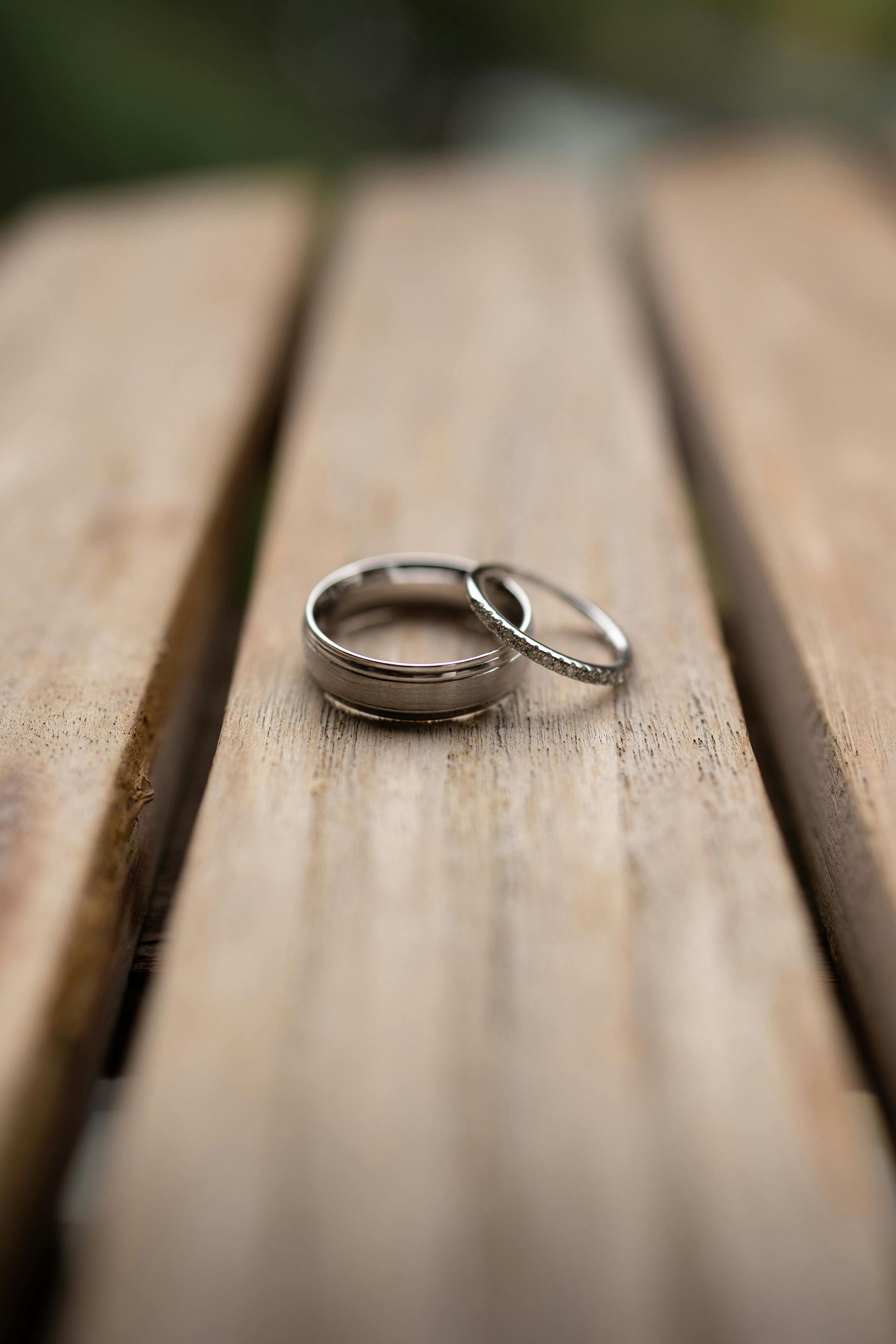 Two wedding rings are sitting on a wooden table.