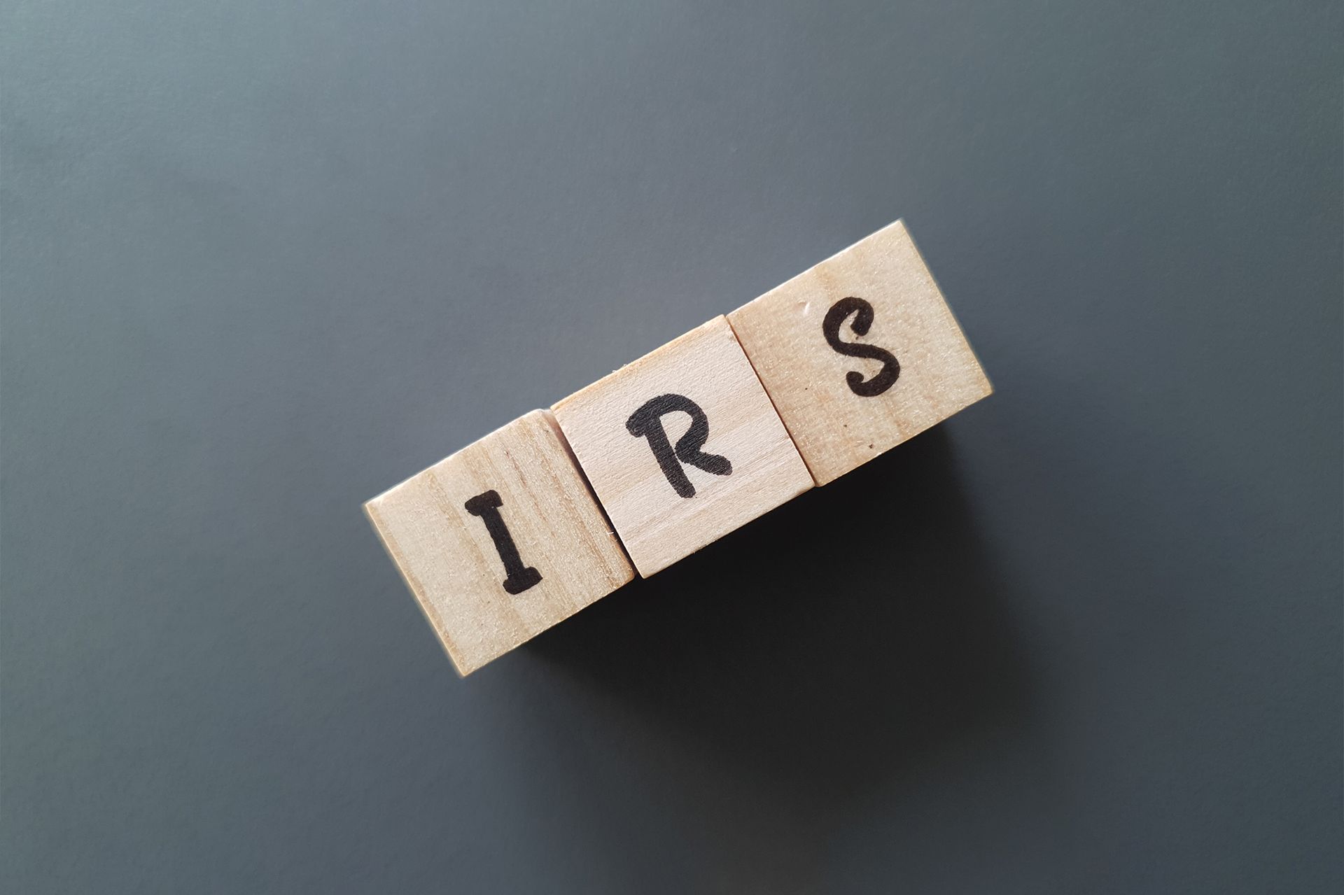 Wooden letter blocks spelling “IRS” on a dark gray surface.
