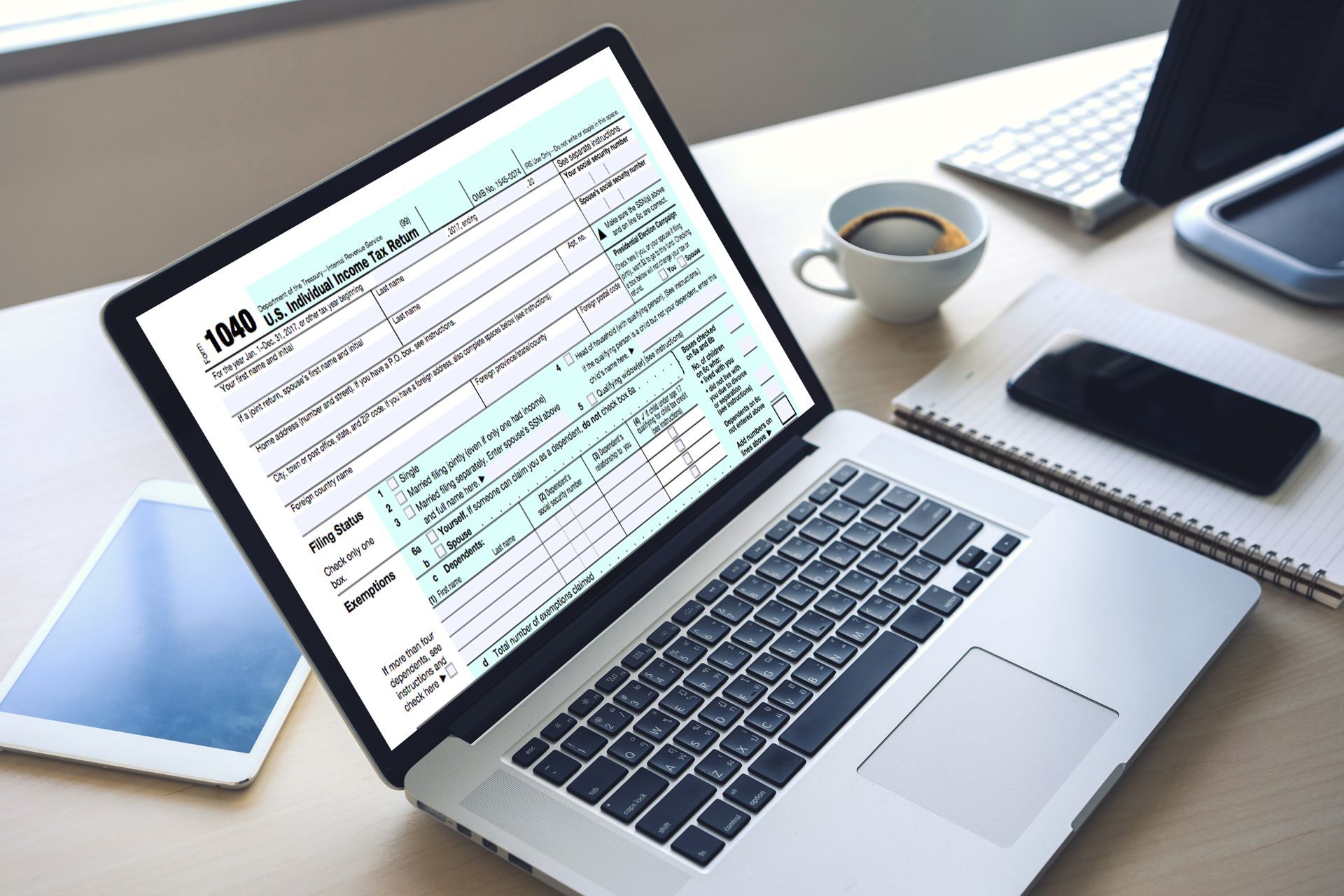 Laptop displaying a spreadsheet on a desk with coffee, phone, keyboard, and tablet nearby