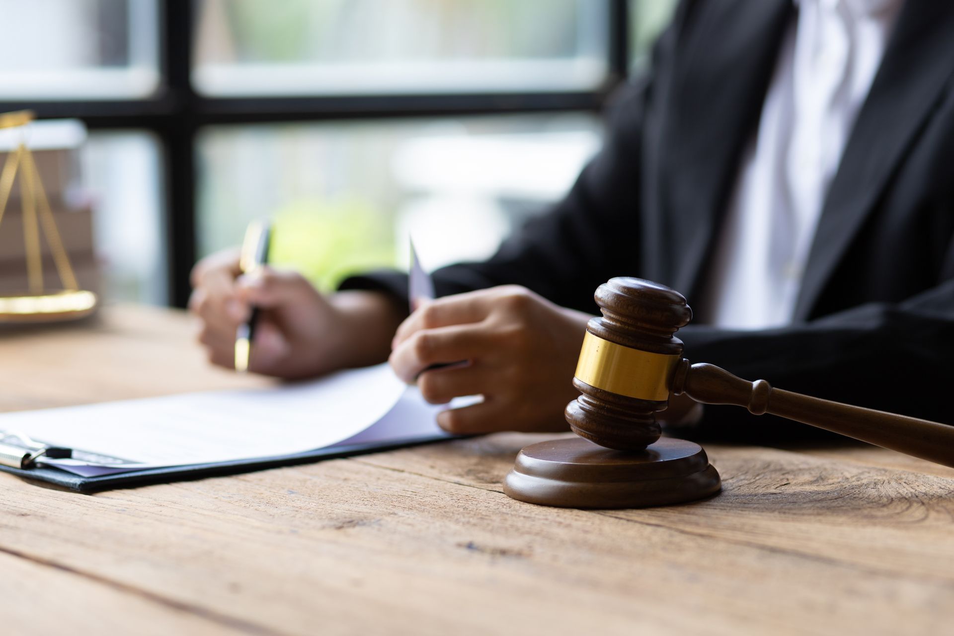 Judge’s gavel on a desk beside a person writing notes in a courtroom office