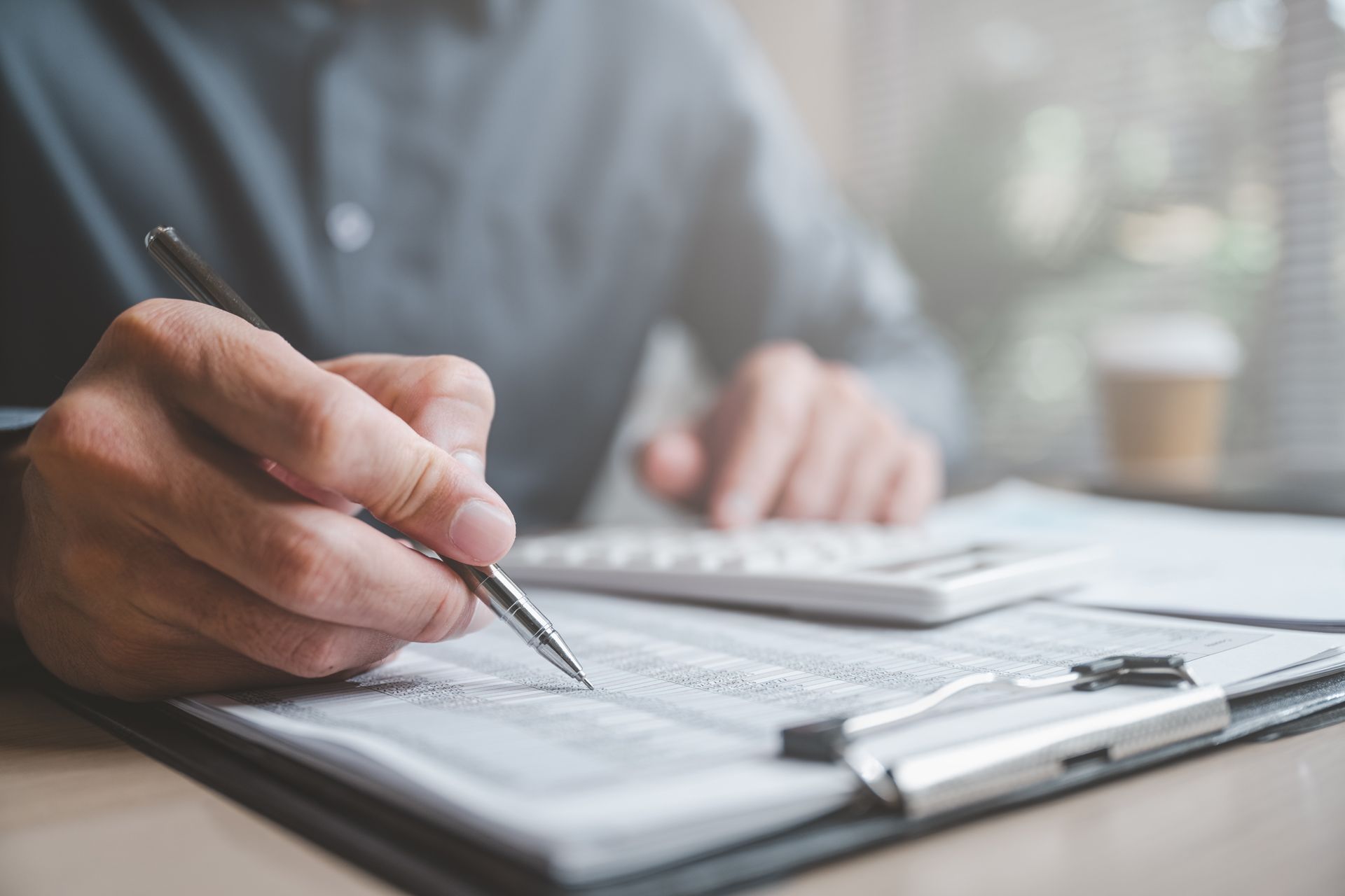 Hand writing on a clipboard beside a calculator at a desk