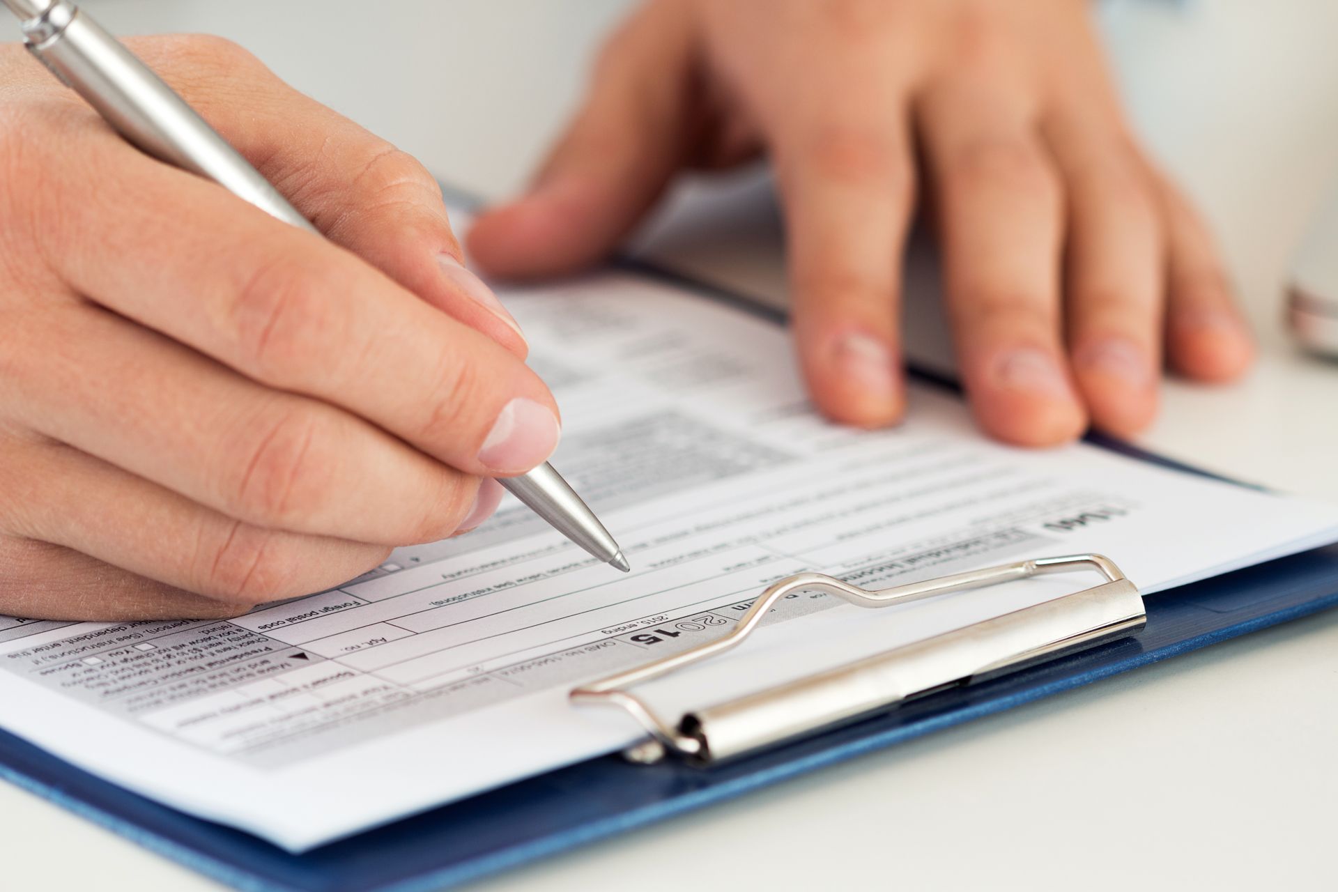 Hand filling out a form on a clipboard with a pen