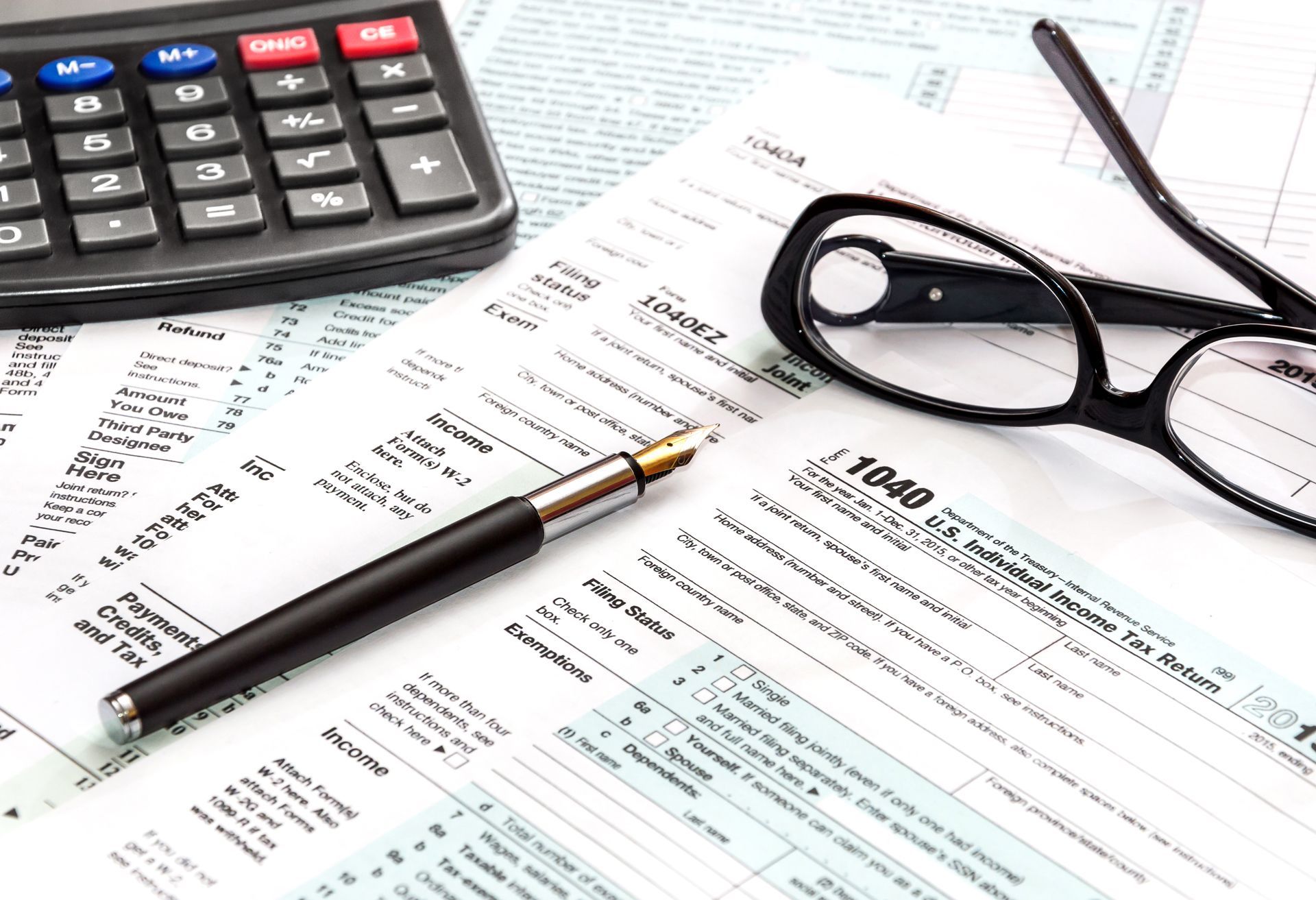 Calculator, glasses, pen, and financial papers on a desk with a laptop in the background