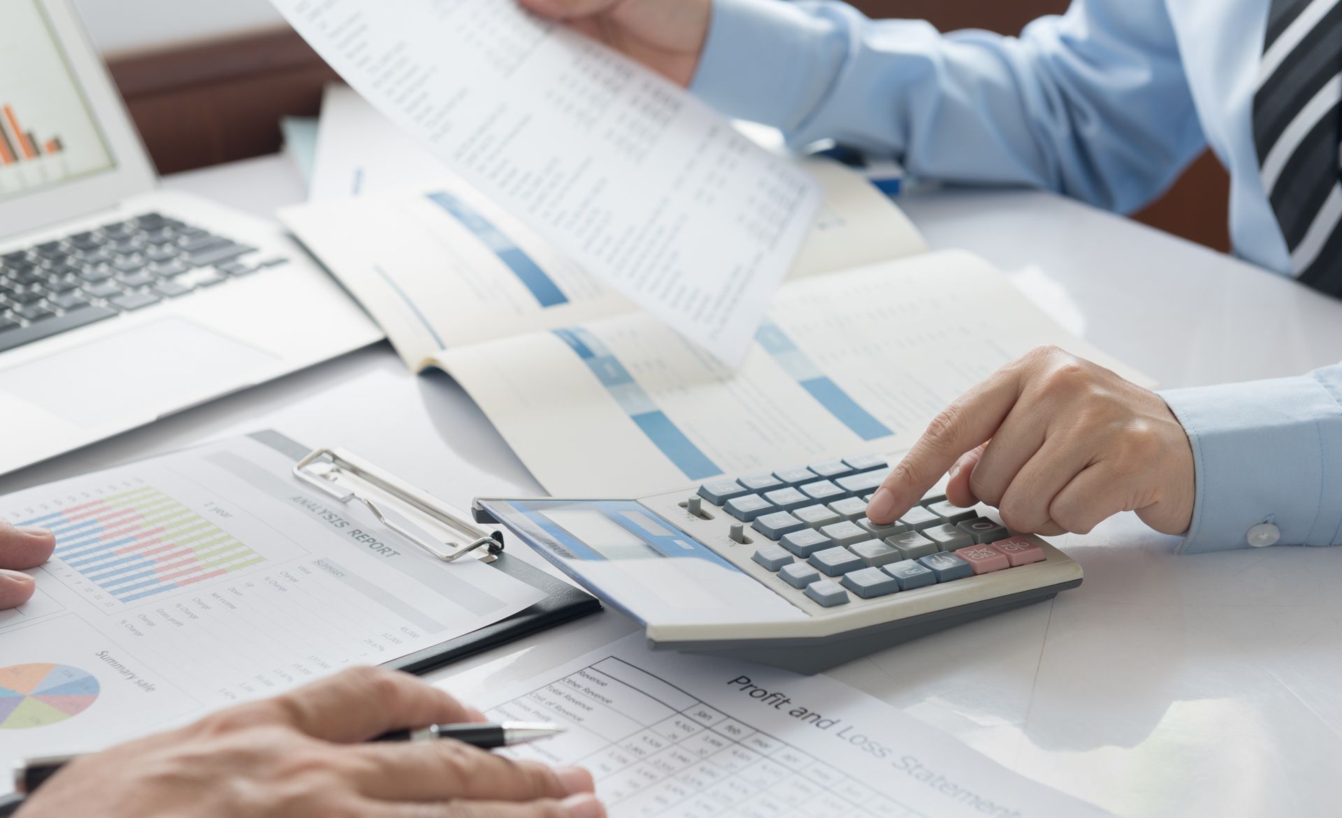 Hands using a calculator over financial charts and papers at a desk