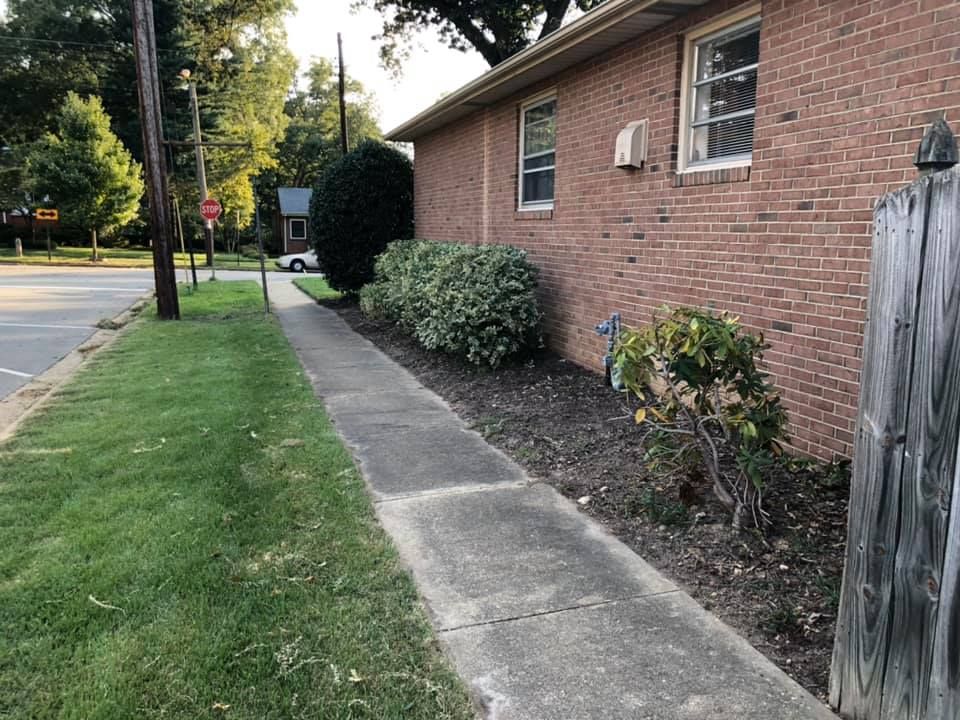 A sidewalk leading to a brick building with a wooden fence.