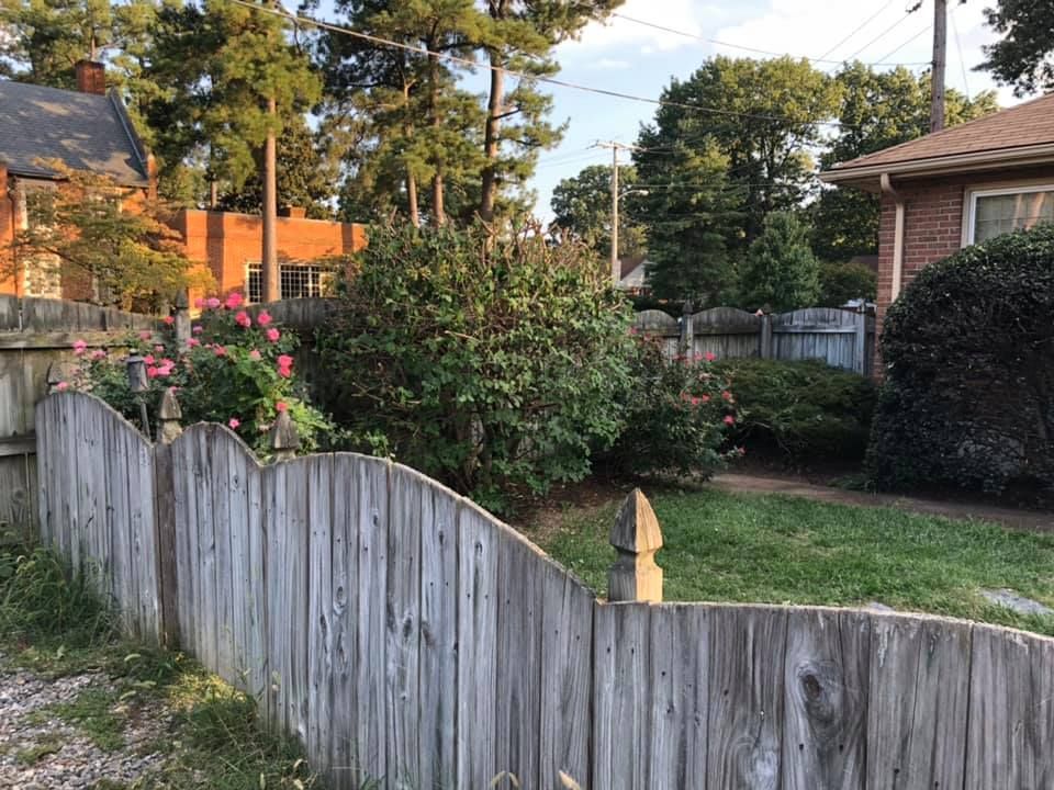 A wooden fence surrounds a lush green yard in front of a brick house.