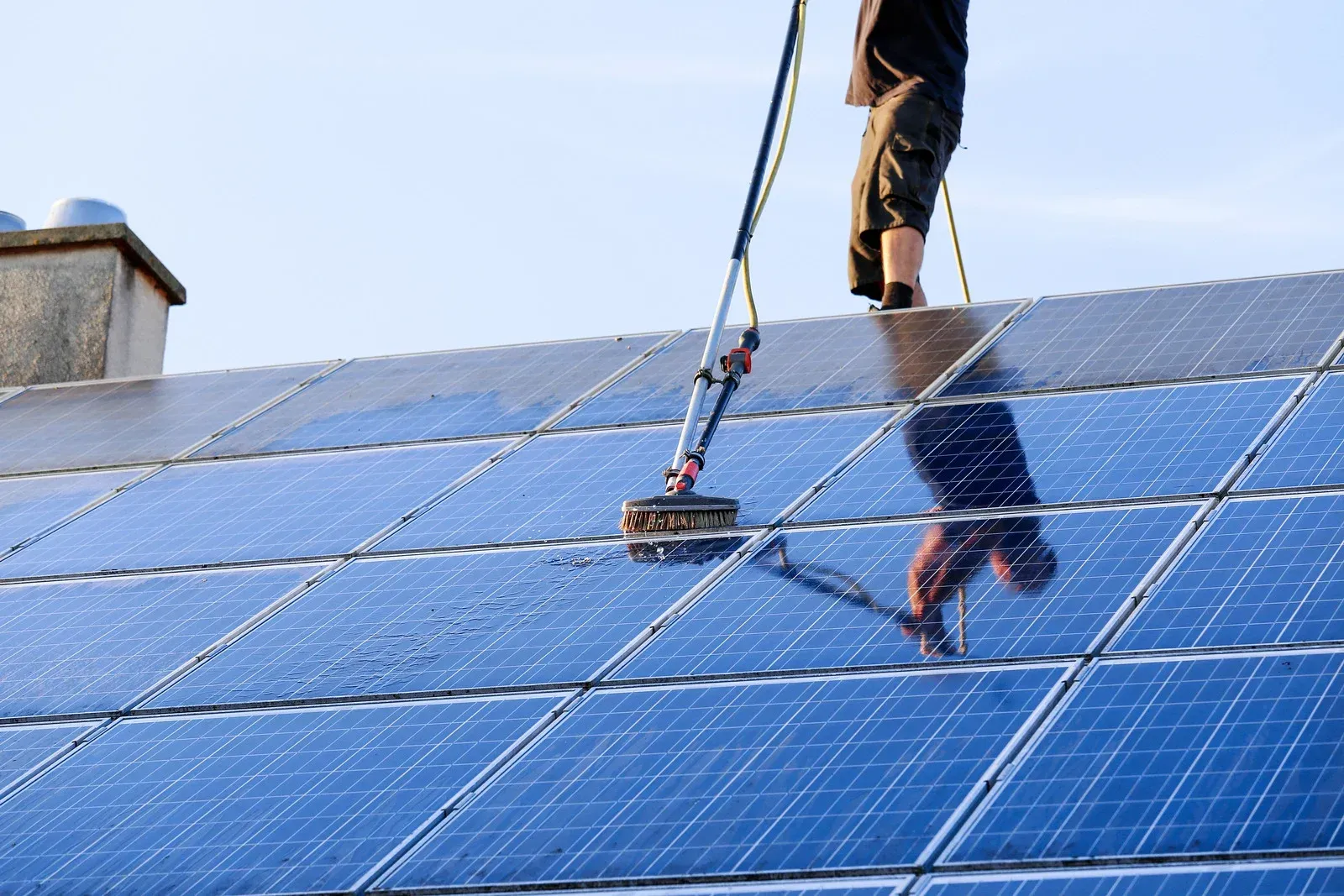 A man is cleaning solar panels on the roof of a building.