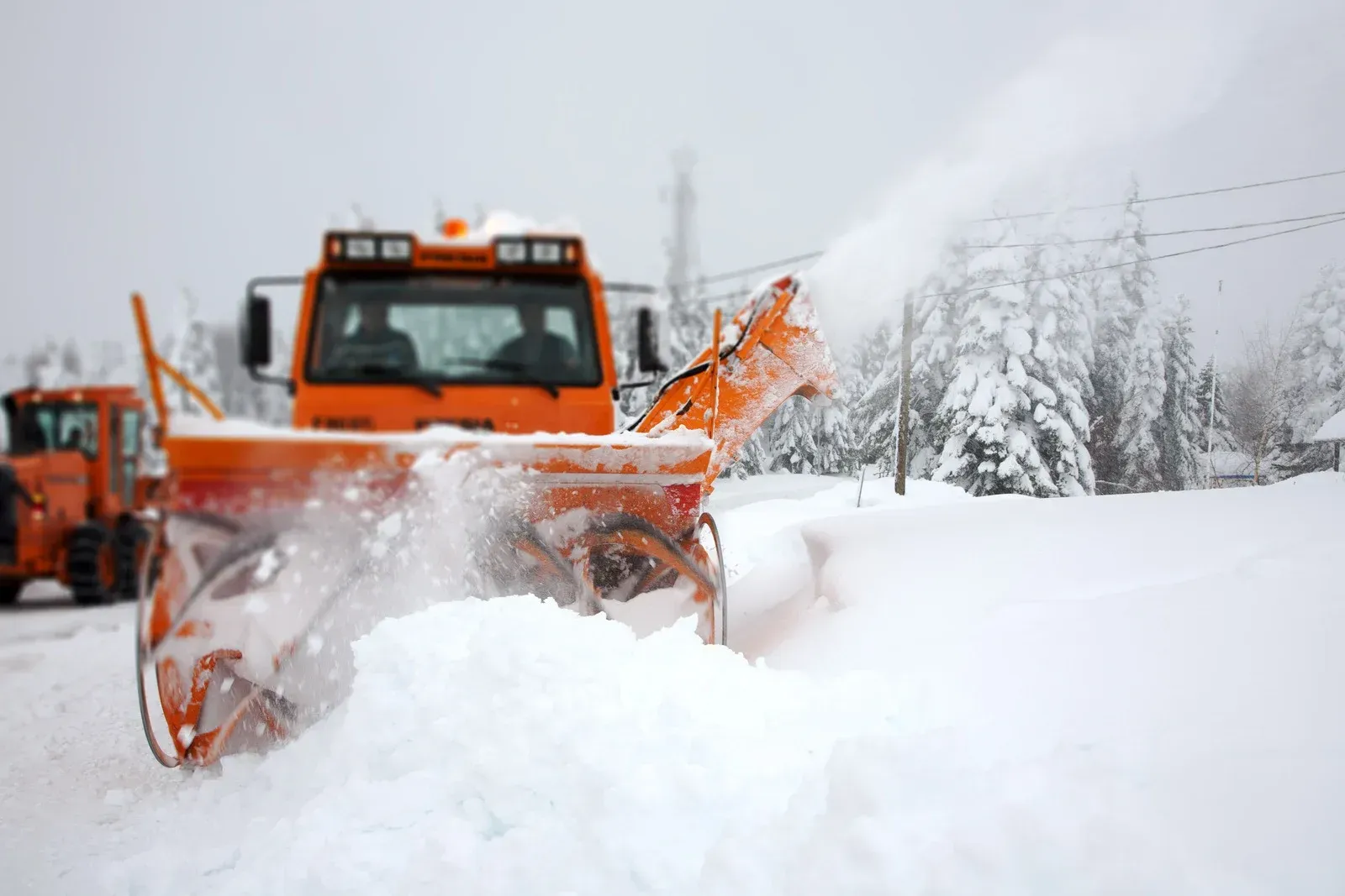 An orange snow plow is clearing a snowy road.