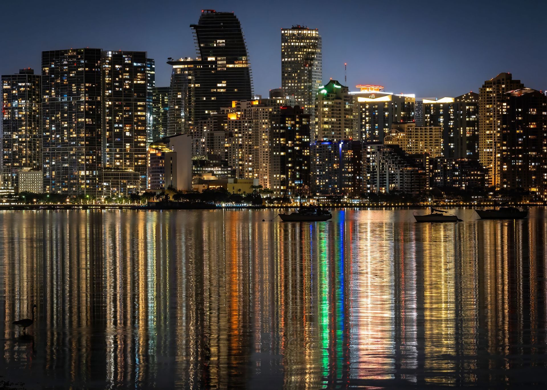 Nighttime city skyline with lit high-rise buildings reflecting across calm water
