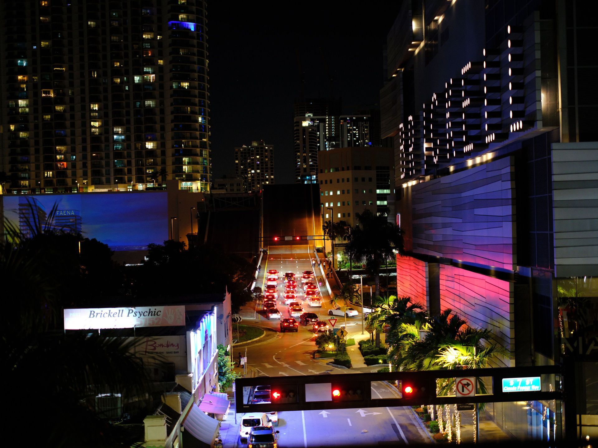 Night city street with traffic, bright building lights, and illuminated signs between tall towers