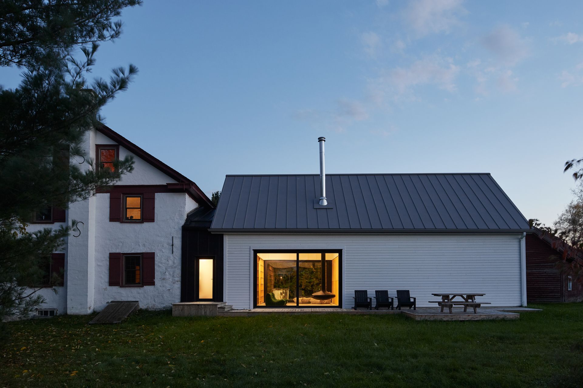 Une maison blanche avec un toit noir et une table de pique-nique devant.