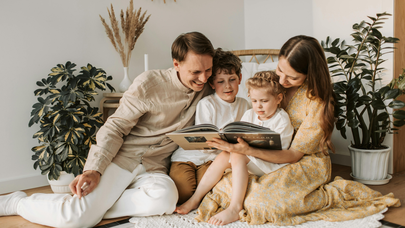 Family looking at a photo album together, sitting on the floor in a living room.