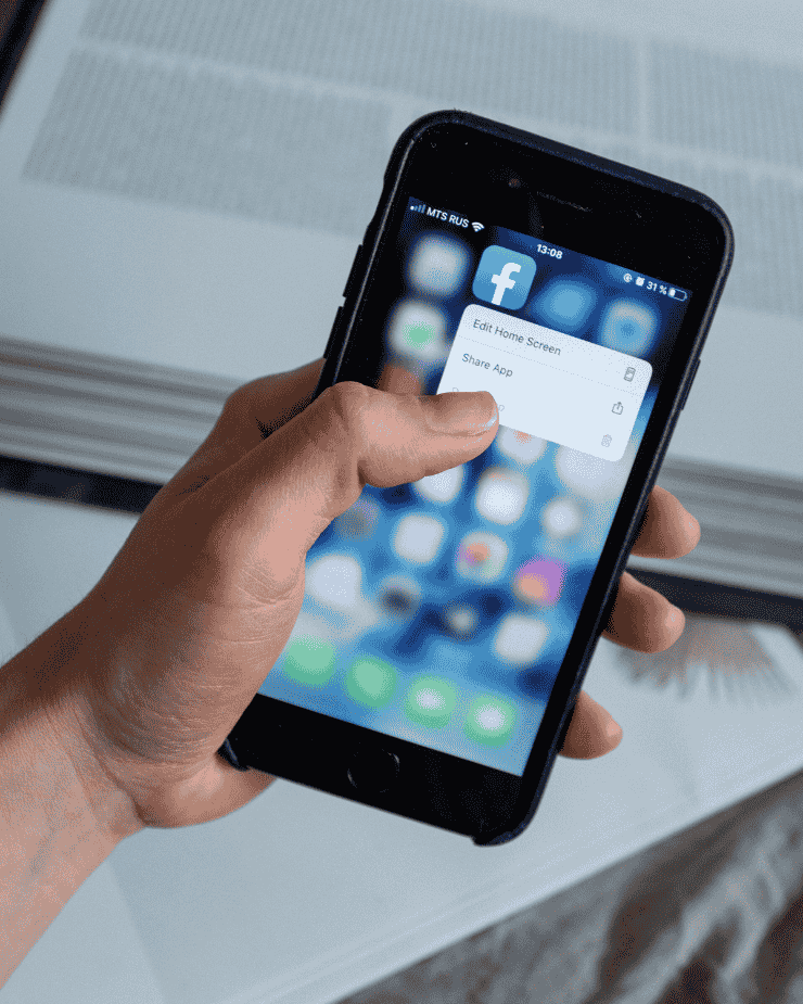 Una persona sostiene un teléfono celular con un icono de Facebook en la pantalla.