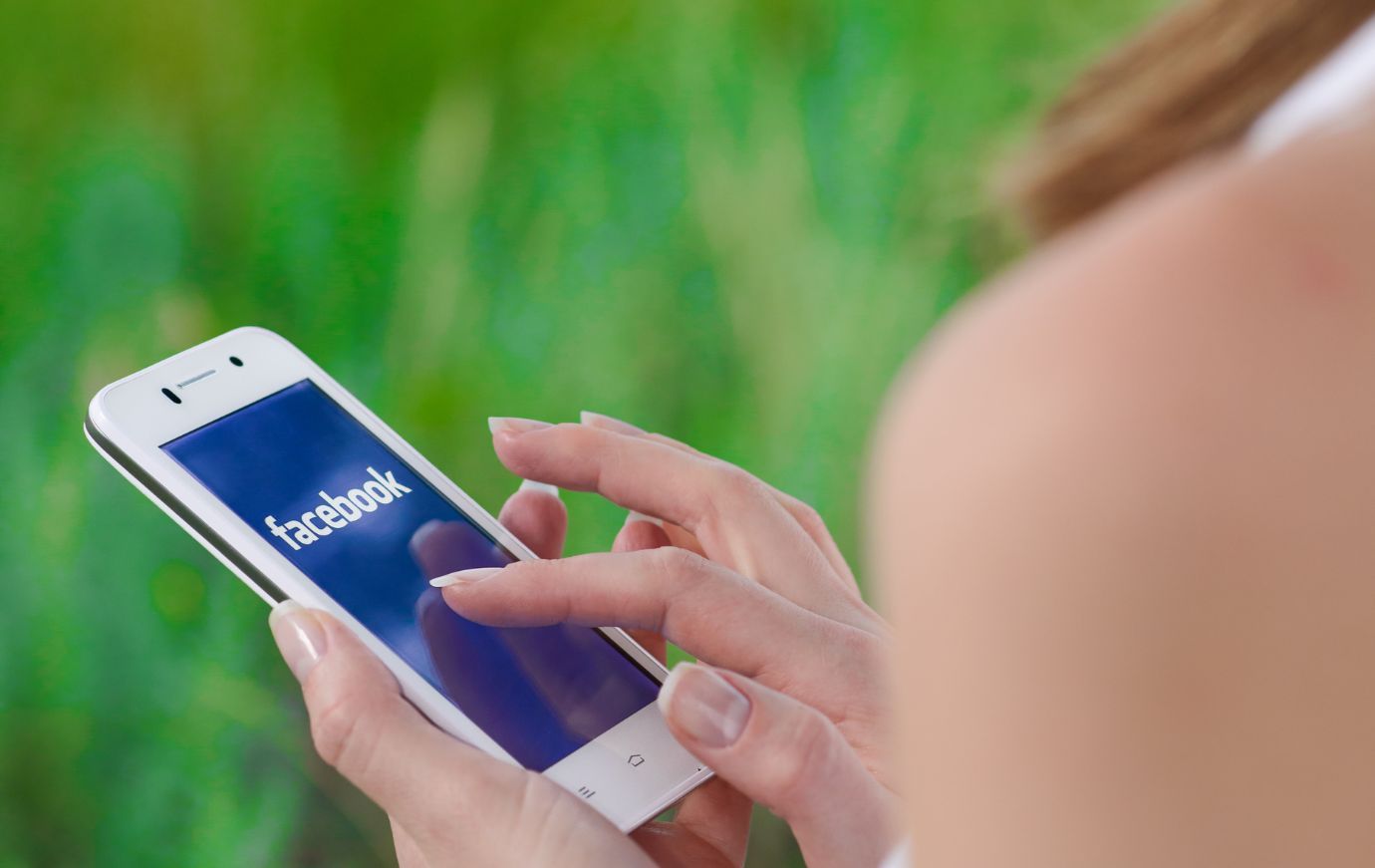 Manos de mujer sosteniendo un teléfono, tocando la pantalla de la aplicación de Facebook