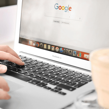 Una persona está escribiendo en una computadora portátil con Google en la pantalla.