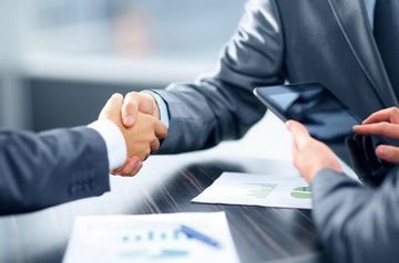 A man and a woman are shaking hands over a table .