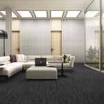 Modern living room with white sectional sofa, gray ottoman, black chairs, and large windows looking outside