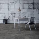 Minimalist dining room with white table, metal chairs, and pendant light against a gray brick wall.
