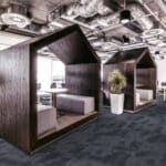 Modern hotel booth-style sleeping pod with bed, wood paneling, and potted plant in a contemporary lounge area