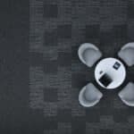 Top-down view of a small gray robot toy on a dark patterned floor