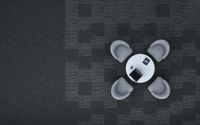 Small white robot toy on a dark patterned carpet, viewed from above.