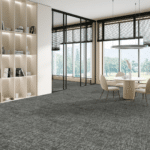 Modern lobby with gray carpet, glass walls, built-in shelving, and a small round table with chairs.