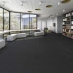 Modern living room with gray sofas, dark carpet, large windows, and a bookshelf wall
