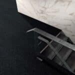 Black metal railing beside a dark carpeted floor and white marble wall corner