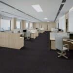Empty modern office with beige desks, white walls, and dark carpet under bright overhead lighting