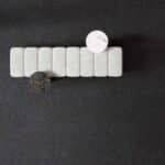 White pill organizer with a small white round tablet on top and a dark clip below on a black background