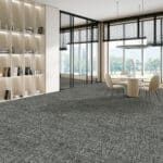 Modern office lounge with gray carpet, glass walls, shelving, and a city view