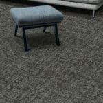 Small gray upholstered stool with black legs on a carpeted floor