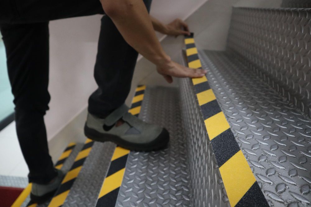 A person applying yellow and black hazard warning tape to the edge of a metal staircase.