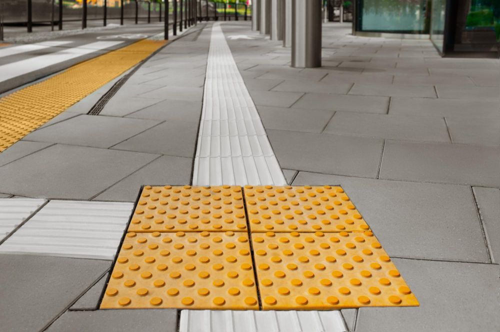 Tactile paving tiles at a sidewalk crossing with yellow warning strips and white guide tiles