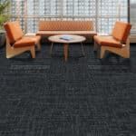 Orange chairs and a round table on a dark carpet in a lobby seating area
