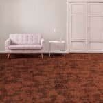 Small white sofa and side table against a pale wall in a mostly empty room with a reddish-brown carpet.