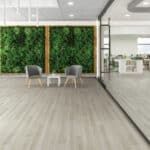 Modern office lounge with gray chairs, small table, wood flooring, and a green plant wall